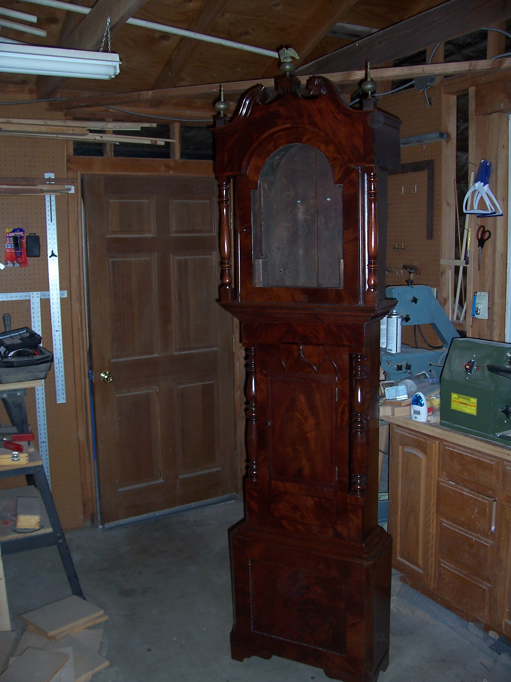 A tall grandfather clock stands in a room beside a wooden workbench